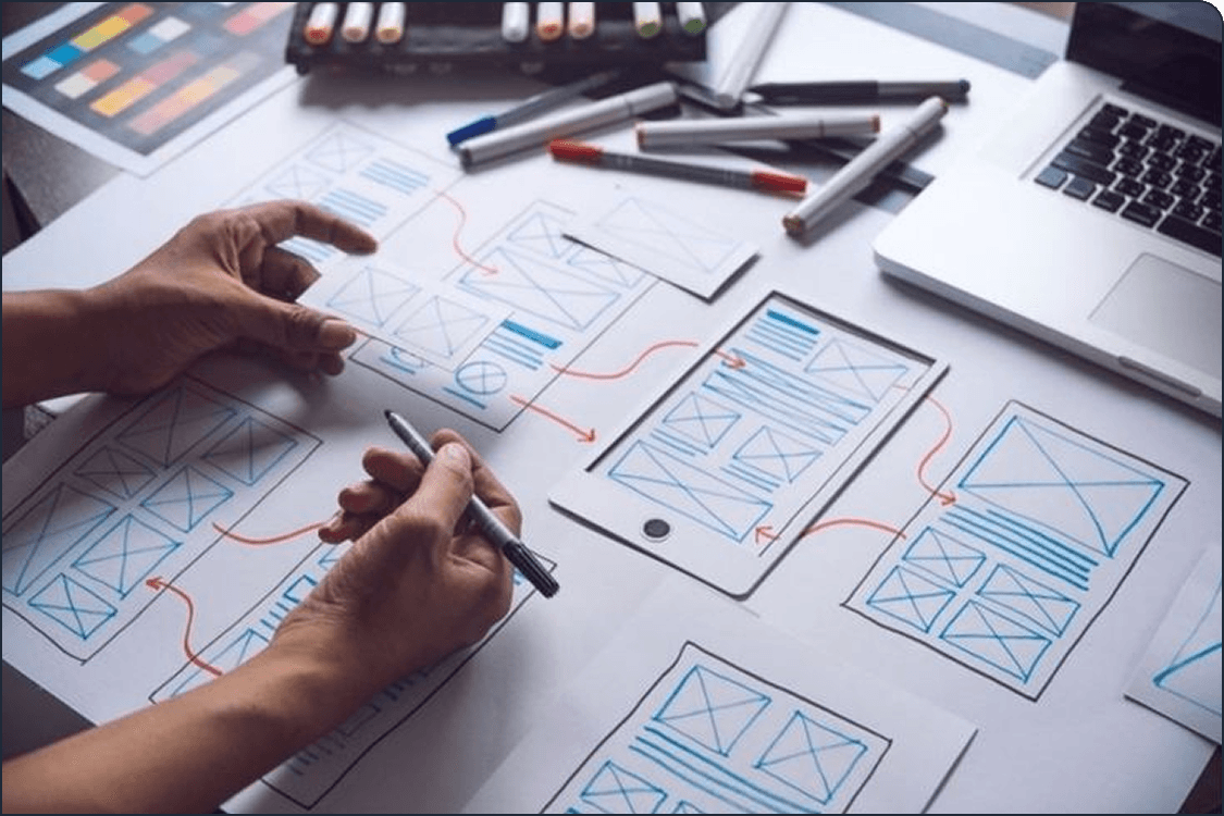 Hands sketching UI wireframes on paper with design tools